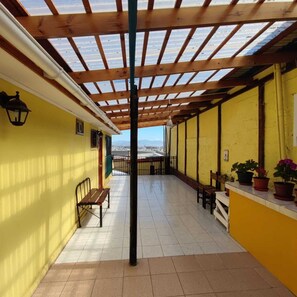 Un balcone coperto con vista sulla città, pareti gialle e piante in vaso.