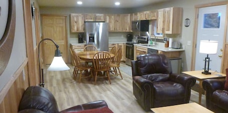 A compact kitchen with wooden cabinets, a refrigerator, microwave, and a dining area with a table and chairs.