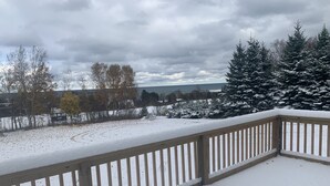 Une terrasse enneigée avec une rambarde en bois, une vue sur un paysage hivernal et une étendue d’eau au loin.