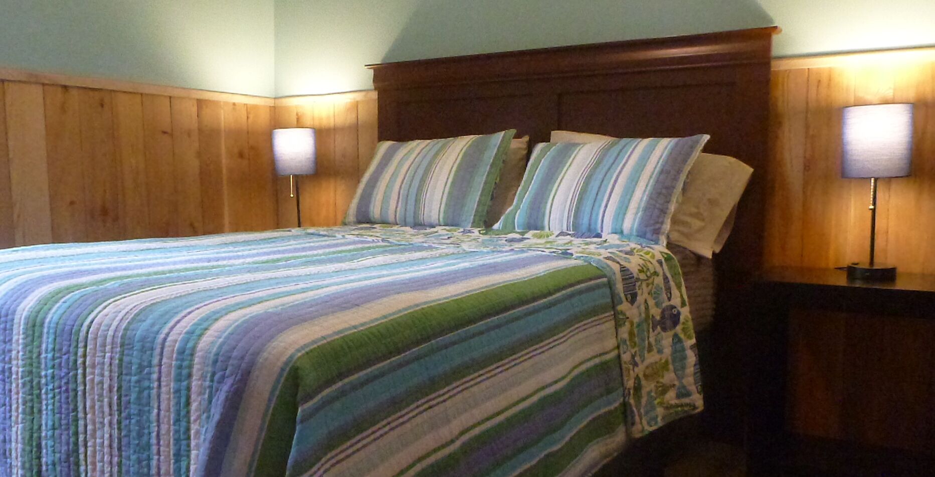 A bed with a striped bedspread, wooden headboard, and two bedside lamps.