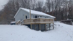 Une maison à deux étages dotée d’une terrasse en bois et d’un porche avant couvert.