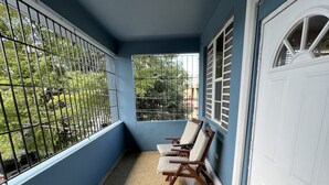 Un balcon donnant sur un espace verdoyant, une porte blanche et deux chaises en bois.