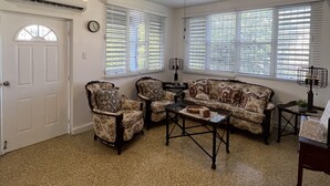 Un salon doté d’un ventilateur de plafond, d’une cheminée et d’une grande fenêtre avec des stores.