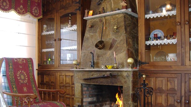 Una chimenea de piedra tradicional con fuego, muebles de madera y estantes con diversos objetos.
