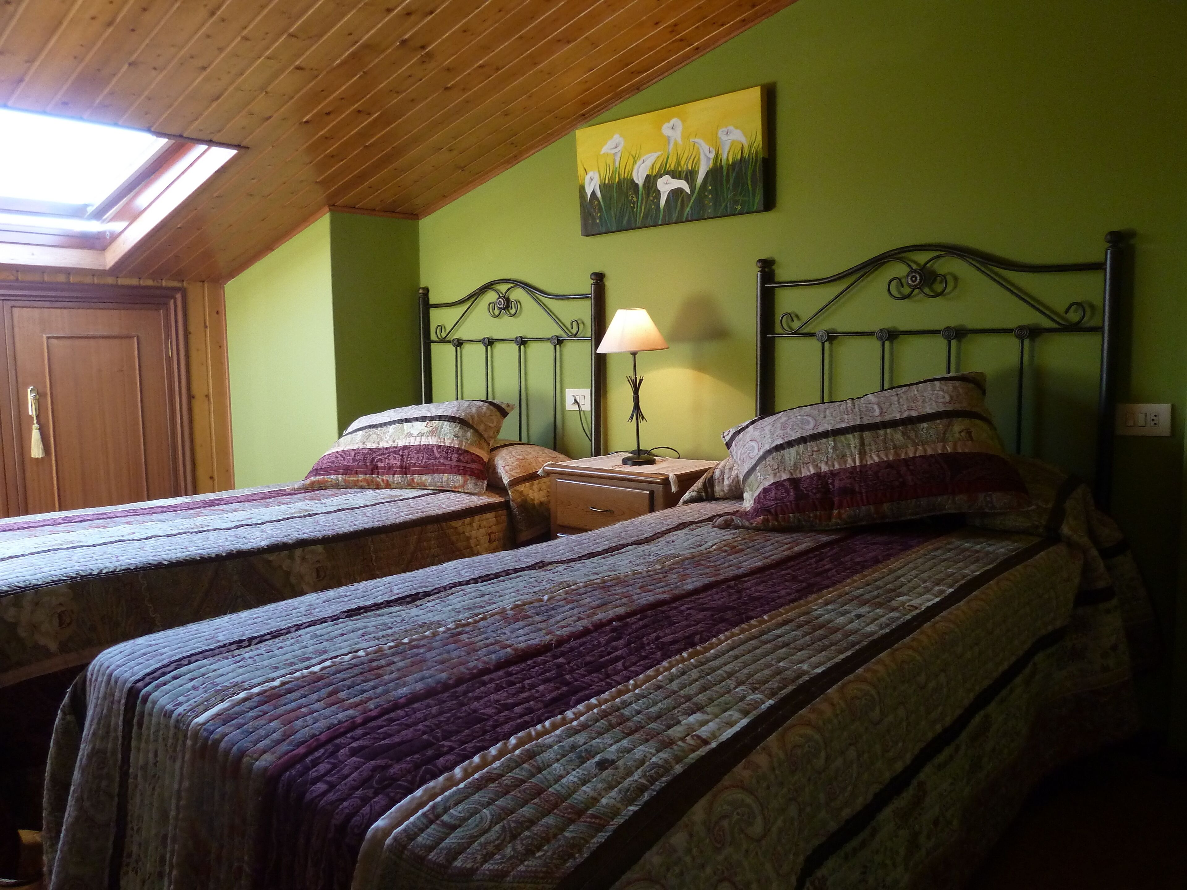 A bedroom with two single beds, a wooden ceiling, a green wall, and a painting of flowers.