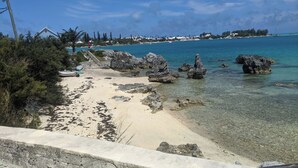 Une plage avec une eau turquoise et limpide, des affleurements rocheux et un mur de pierres.
