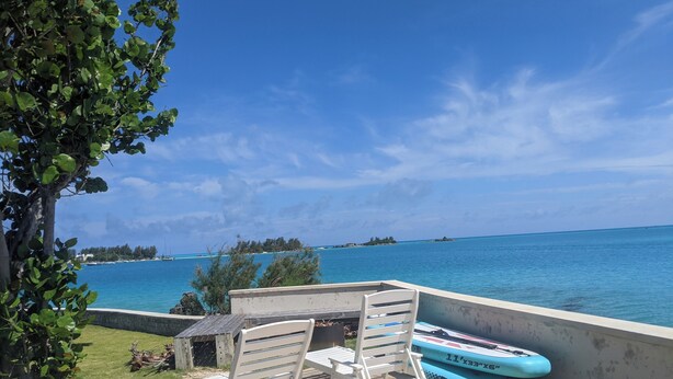 Une terrasse avec vue sur l’océan, une chaise longue, une petite table et un bateau.