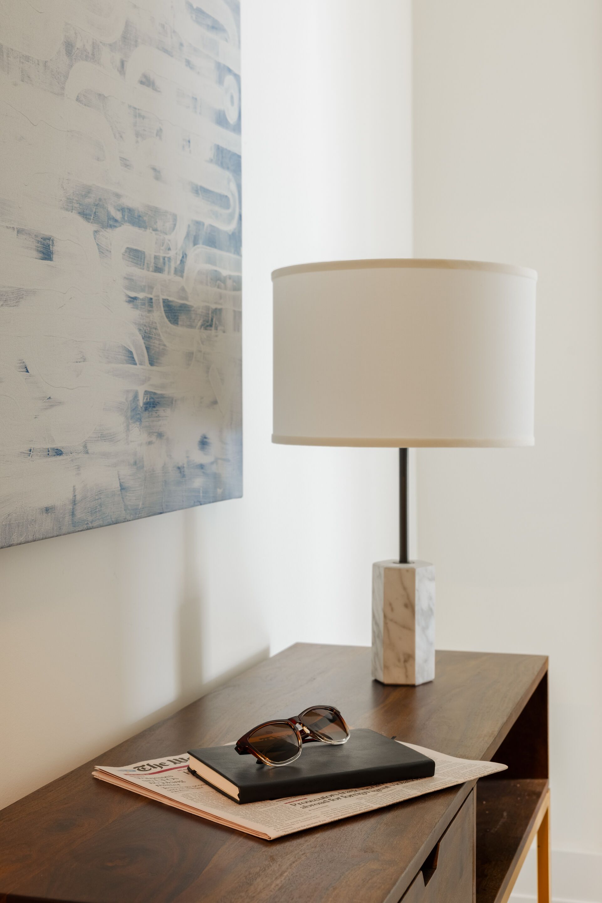 A wooden nightstand with a lamp, a book, and glasses.