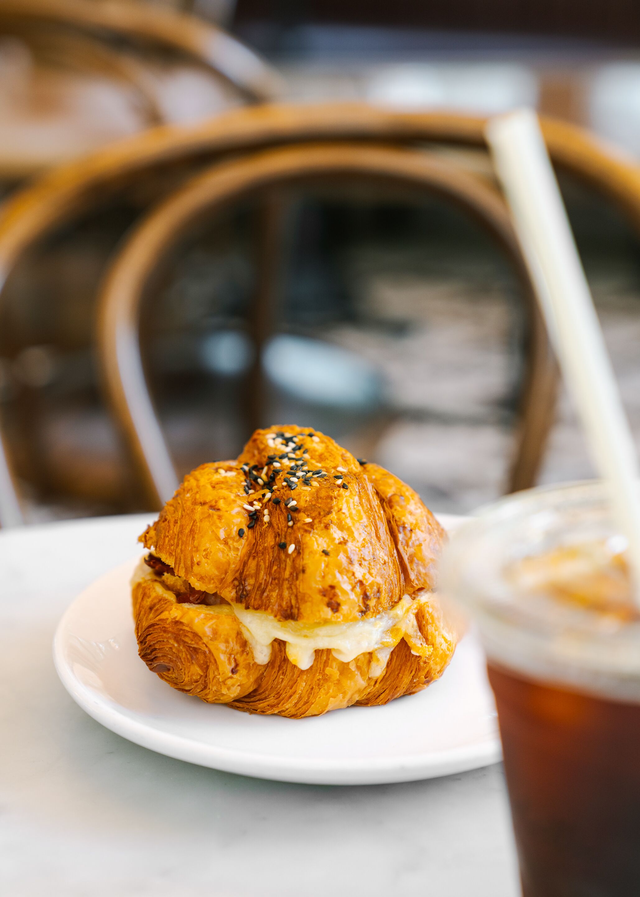A croissant sandwich on a white plate with a drink in the background.