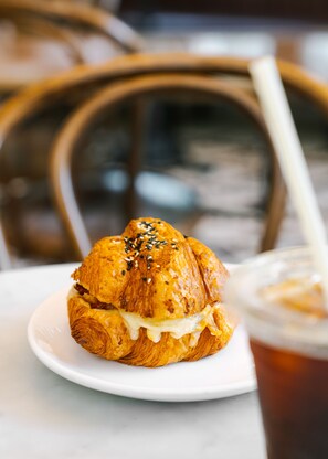 A croissant sandwich on a white plate with a drink in the background. - Reside NoMa, a Wyndham Residence (Washington)