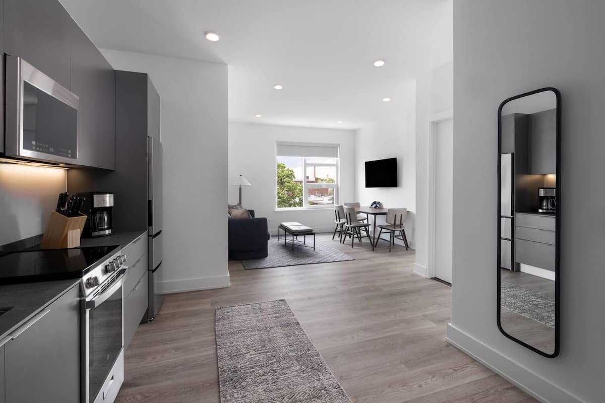 A modern kitchen with built-in appliances, a dining area with a table and chairs, and a large mirror on the wall.