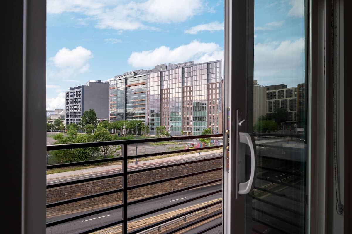 A view from a balcony with a metal railing, overlooking a cityscape with modern buildings and a clear sky.