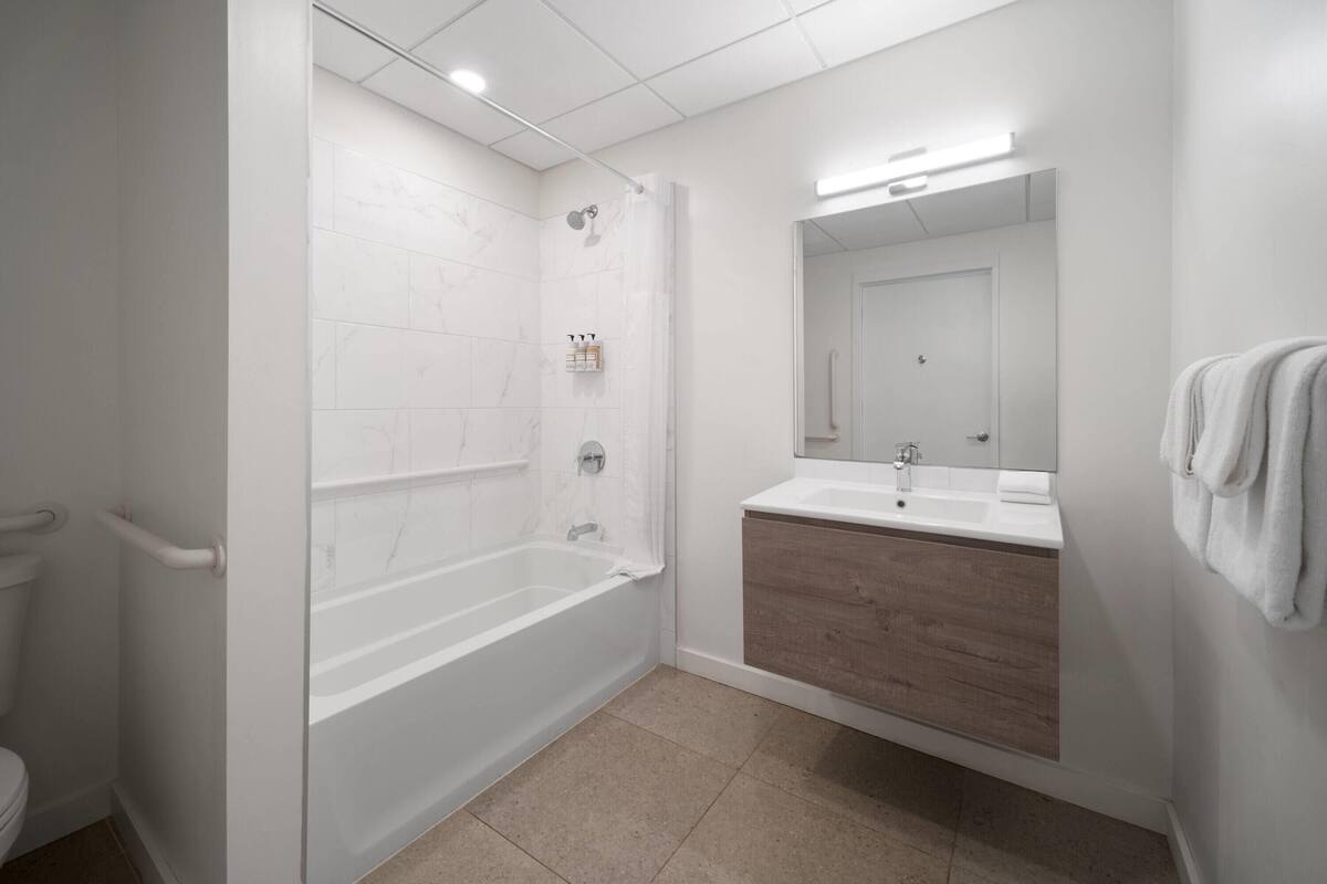 A modern bathroom with a white bathtub, a wooden vanity, and a large mirror.