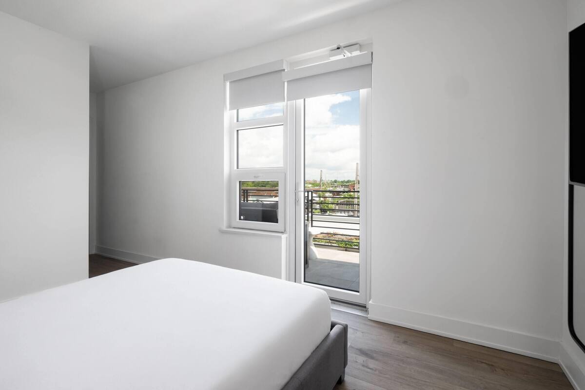 A modern bedroom with a large bed, a sliding glass door leading to an outdoor balcony, and a view of the cityscape.