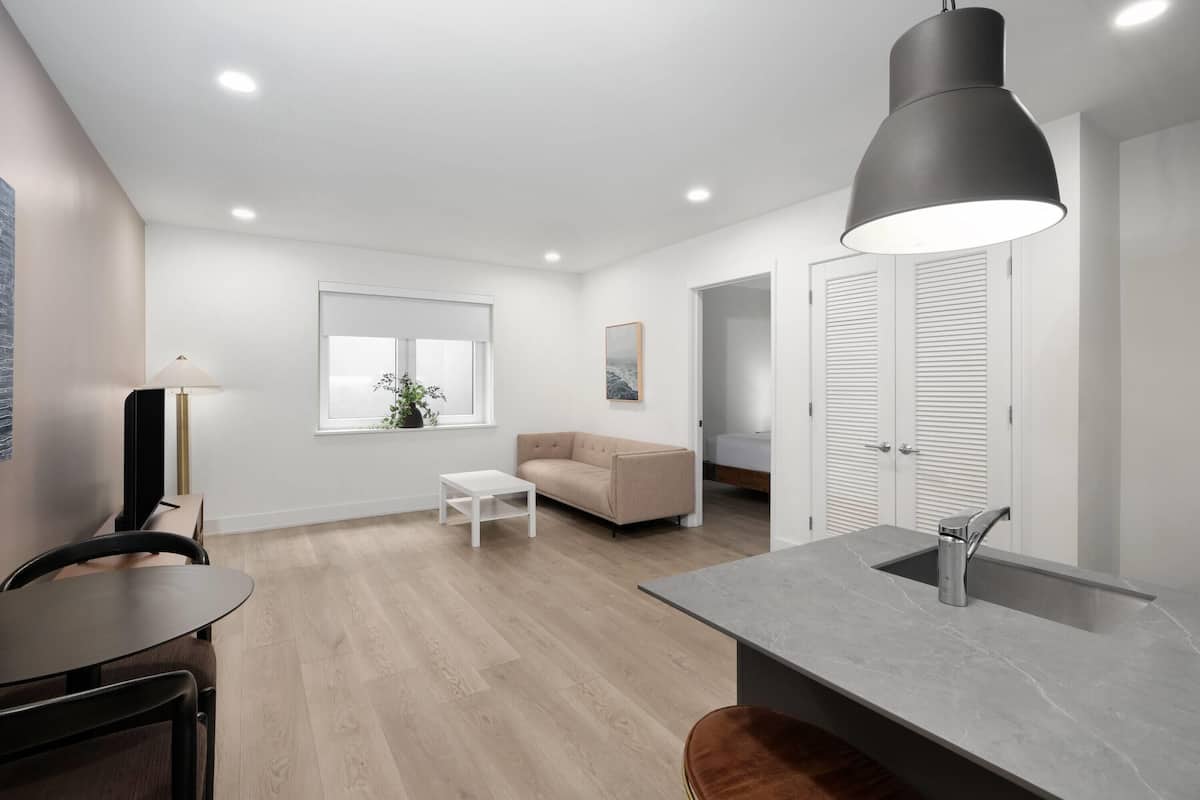 A modern kitchen with a grey countertop and sink, a beige sofa, and a dining area with a table and chairs.
