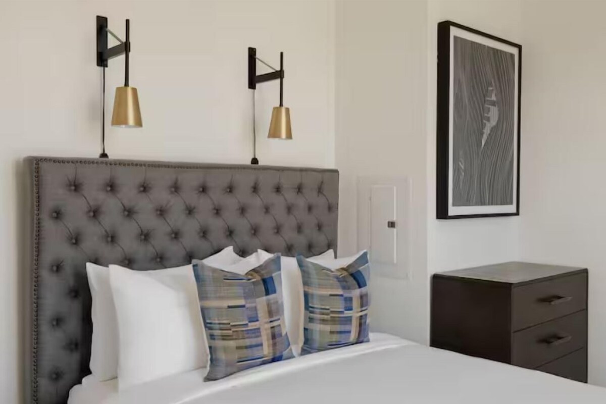 A neatly made bed with a tufted headboard, two bedside lamps, and a framed artwork on the wall.
