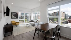 A spacious living area with a large window, a sofa, a coffee table, and a dining table with chairs. - Reside NoMa, a Wyndham Residence (Washington)