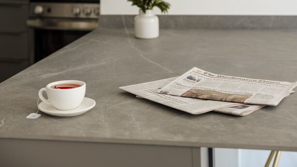 A kitchen counter with a white cup of tea, a newspaper, and a pendant light. - Reside NoMa, a Wyndham Residence (Washington)