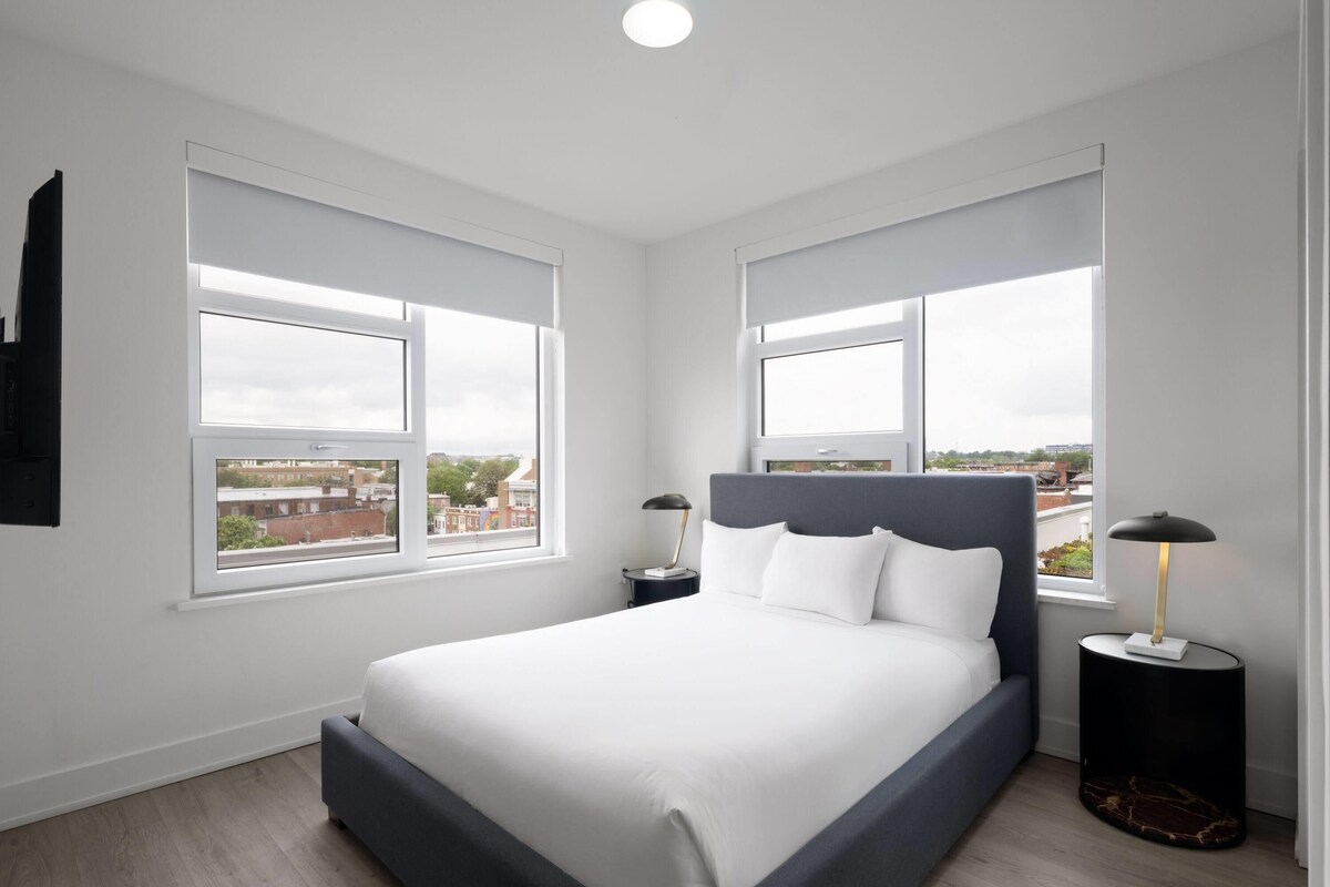 A modern bedroom with a large bed, two bedside tables, and a view of the city through large windows.