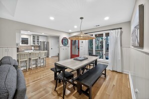Una cocina moderna con armarios blancos, un comedor con mesa y bancos de madera, y un ventanal con cortinas.