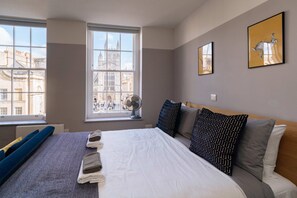 A hotel room with a large bed, a view of a historic building, and two framed artworks on the wall.