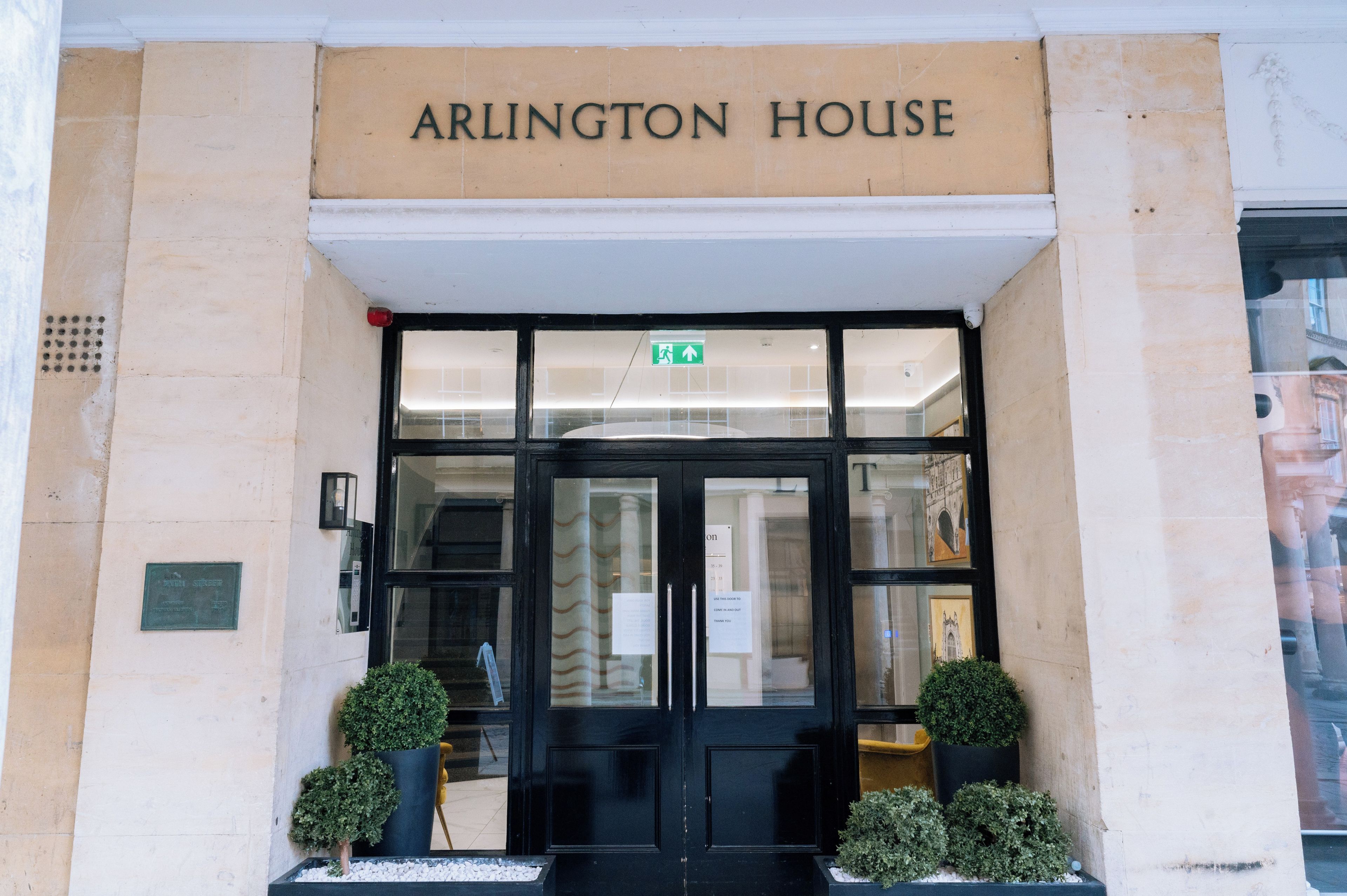 The entrance to Arlington House with a sign above the door, a glass door, and two potted plants on either side.