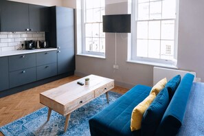 A modern kitchen with grey cabinets, a wooden coffee table, and a blue sofa with cushions. - Stunning Studio Flat with Scenic Views (Bath and North East Somerset)