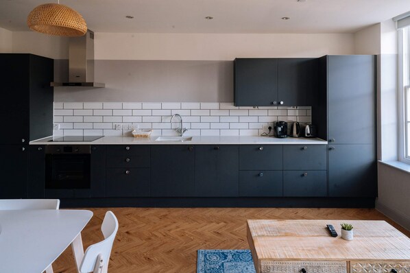 A modern kitchen with dark cabinets, a white countertop, and a herringbone-patterned floor.