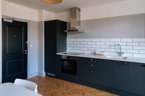 A modern kitchen with dark cabinets, a white countertop, a built-in oven, and a stainless steel range hood. - Stunning Studio Flat with Scenic Views (Bath and North East Somerset)