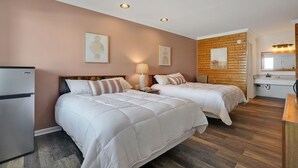 A hotel room with two beds, a refrigerator, a wooden accent wall, and a bathroom with a mirror and sink.