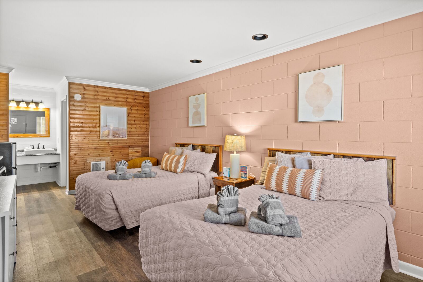 Una habitación de hotel con dos camas, un revestimiento de pared de madera, un lavamanos blanco y un espejo.