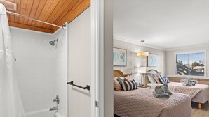 A hotel room with a shower, two beds with matching bedding, a window with a view, and a wooden ceiling.