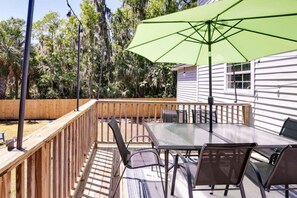 Een terras met een tafel, stoelen, een groene parasol en een houten leuning.