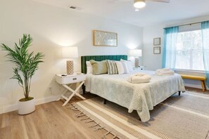 Une chambre à coucher avec un lit, des tables de chevet, une lampe, une plante en pot et une fenêtre avec des rideaux.