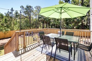 A wooden deck with a glass table and chairs, a green umbrella, and a wooden railing.