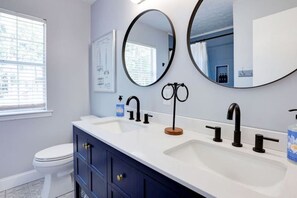 A bathroom with two sinks, a toilet, and two round mirrors.