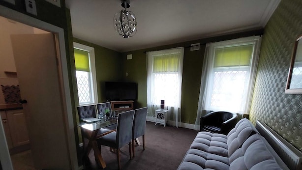 A living room with a sofa, a dining table with chairs, a TV, and a chandelier. - Captivating 1-bed Apartment in Blackpool (Blackpool)