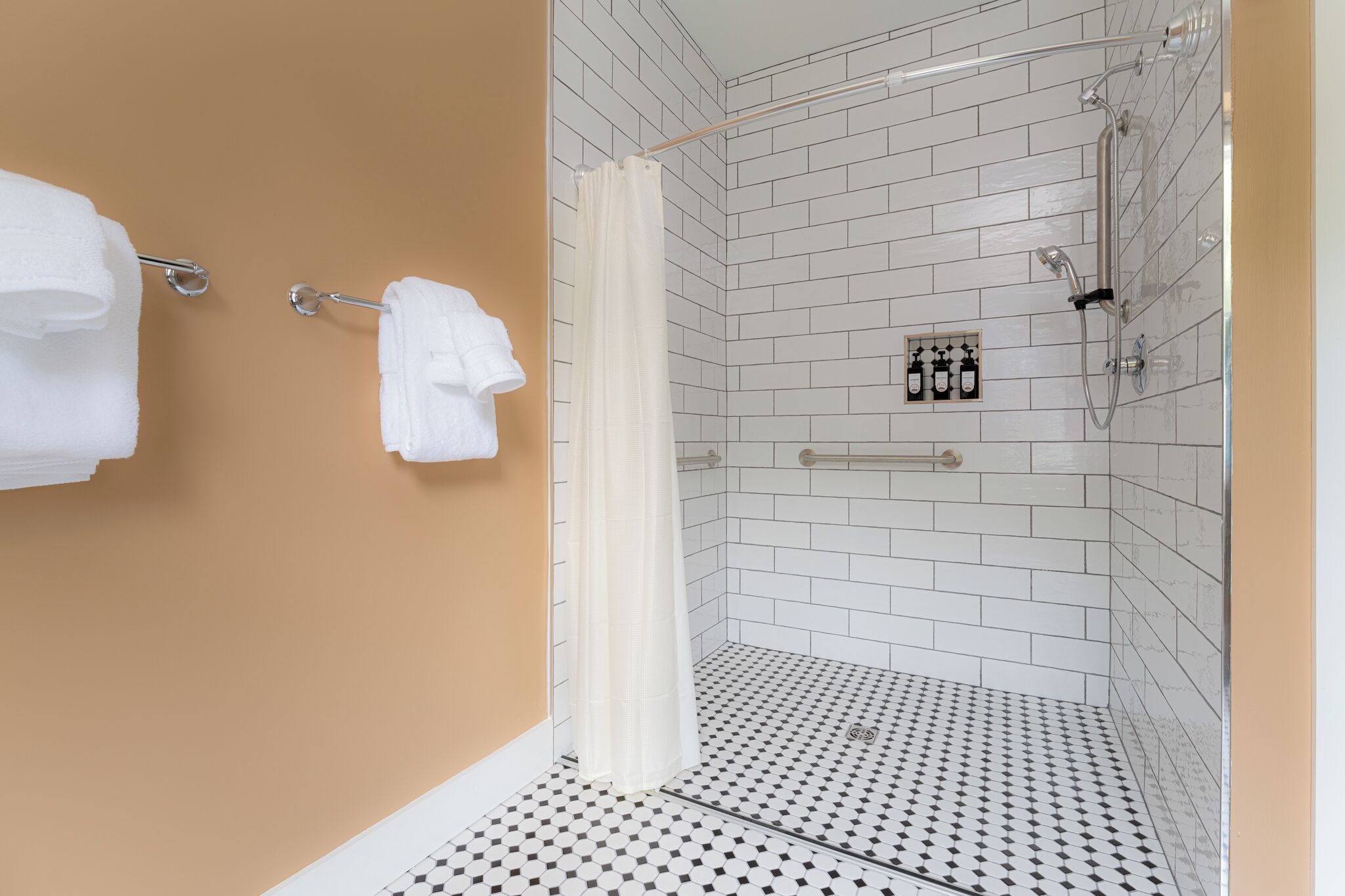 A shower with white tiles, a towel rack, and a showerhead.