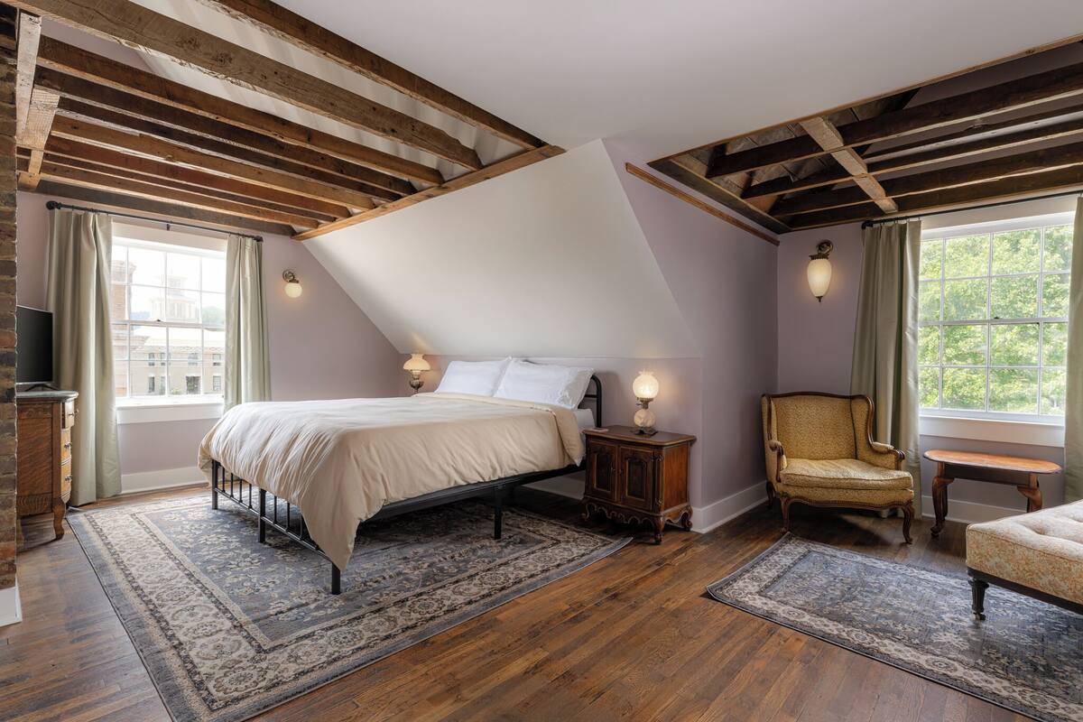 Ein Schlafzimmer mit schrägem Dach, einem Bett, einem Sessel, einem kleinen Tisch und einem Fernseher.