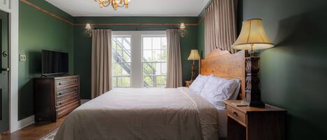 A bedroom with a large bed, wooden dresser, and a television on a dresser.