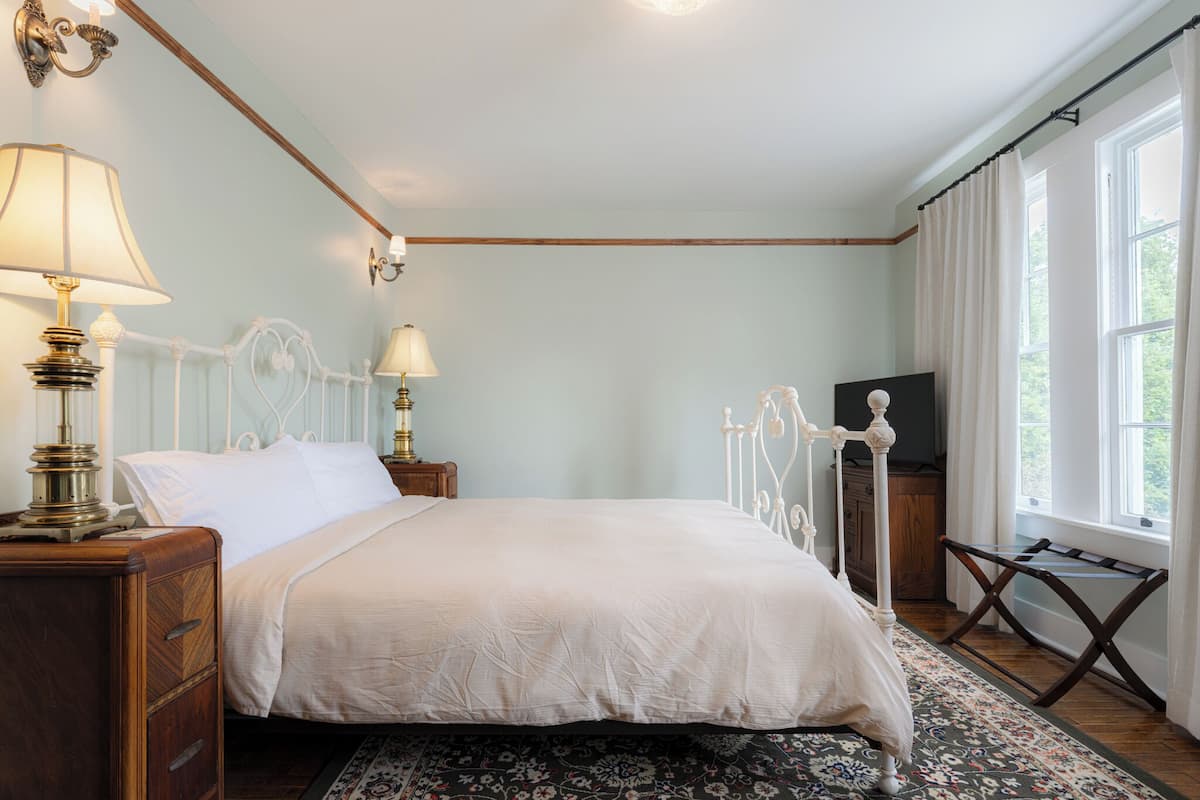 Ein Schlafzimmer mit einem Himmelbett, Nachttischlampen, einem Fernsehschrank und einem Fenster mit Vorhängen.