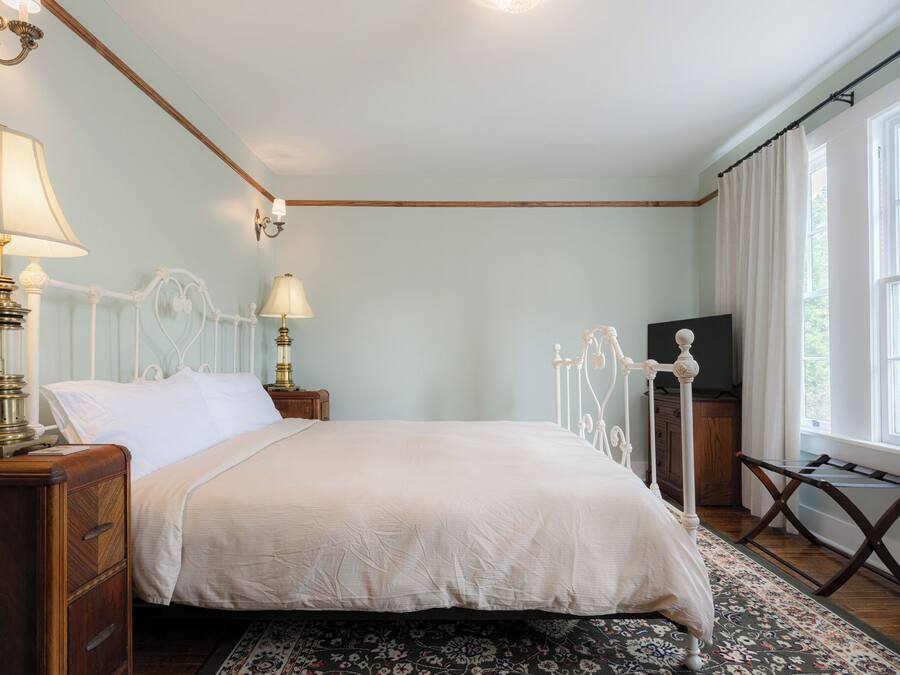A bedroom with a four-poster bed, bedside lamps, a TV stand, and a window with curtains.