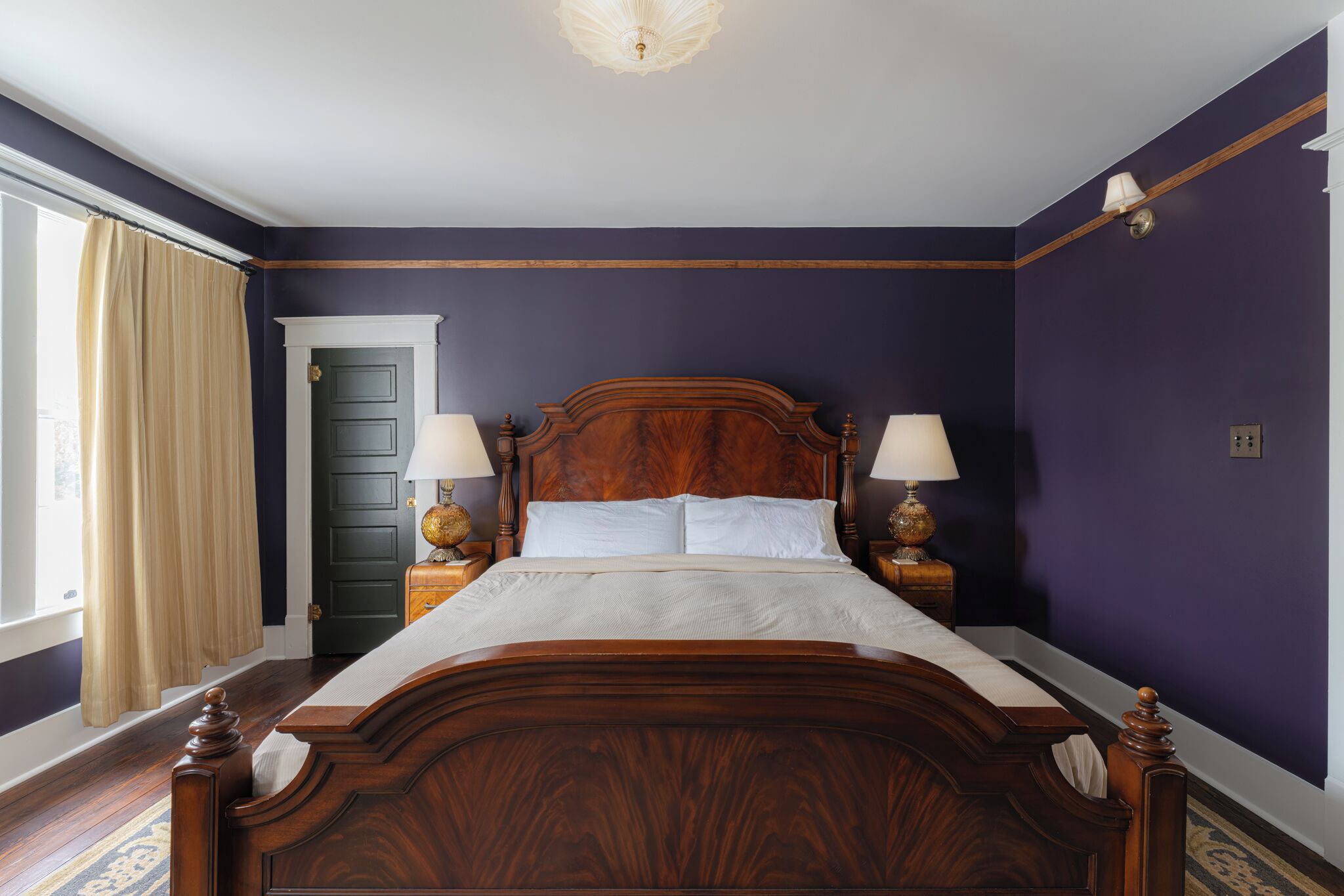 A bedroom with a wooden bed, two bedside lamps, a nightstand, and a door with a curtain.