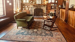 Ein gemütlicher Raum mit einem grünen Sofa, einem Schaukelstuhl, einem Kamin und einem Bücherregal.