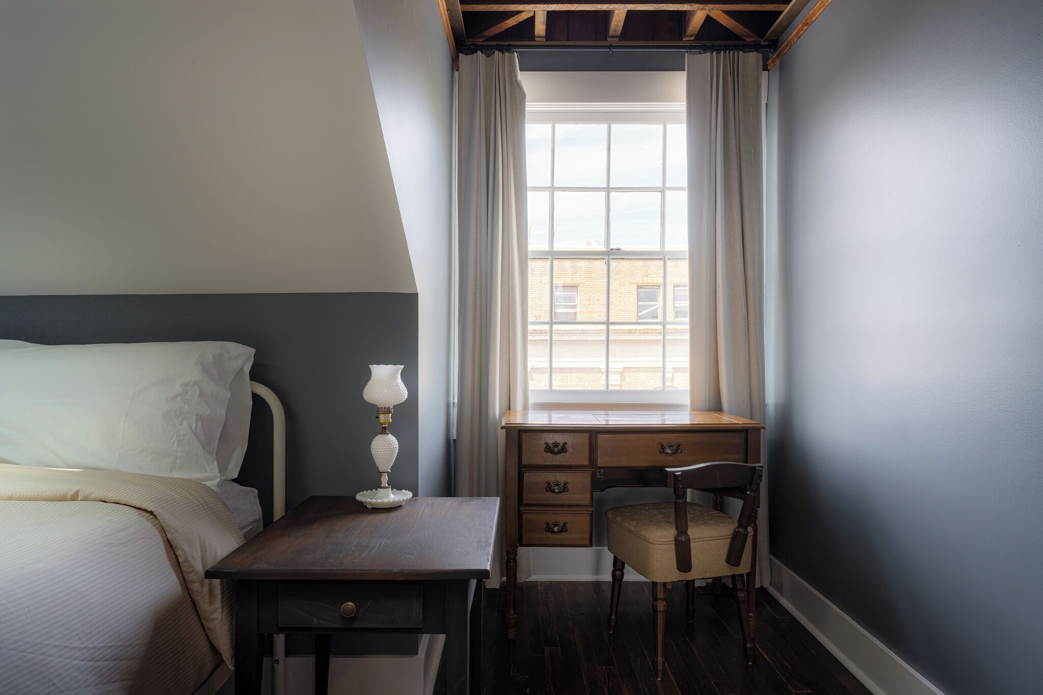 A bedroom with a bed, a desk, a chair, and a window with curtains.