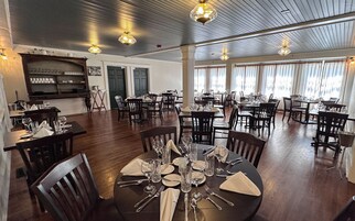 Comedor con varias mesas dispuestas para el servicio, piso de madera e iluminación colgante.