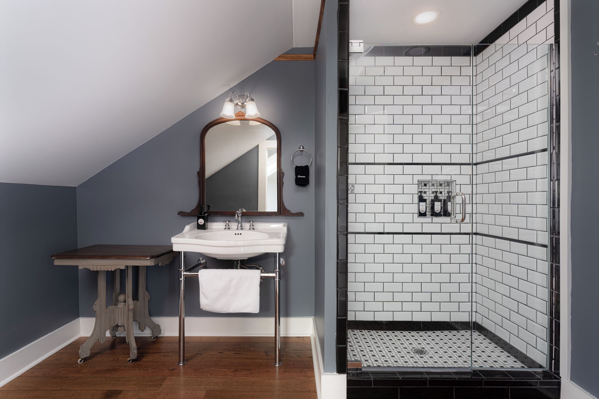 A bathroom with a white sink, wooden vanity, and a tiled shower area.