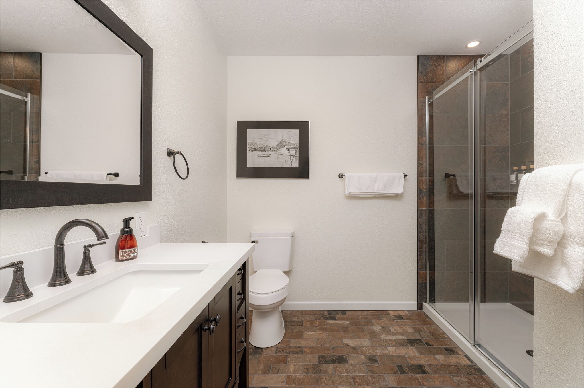 A bathroom with a white sink, a toilet, a shower, and a framed picture on the wall.