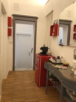 Un pasillo con una puerta blanca, un armario rojo, un espejo y una mesita con objetos encima.
