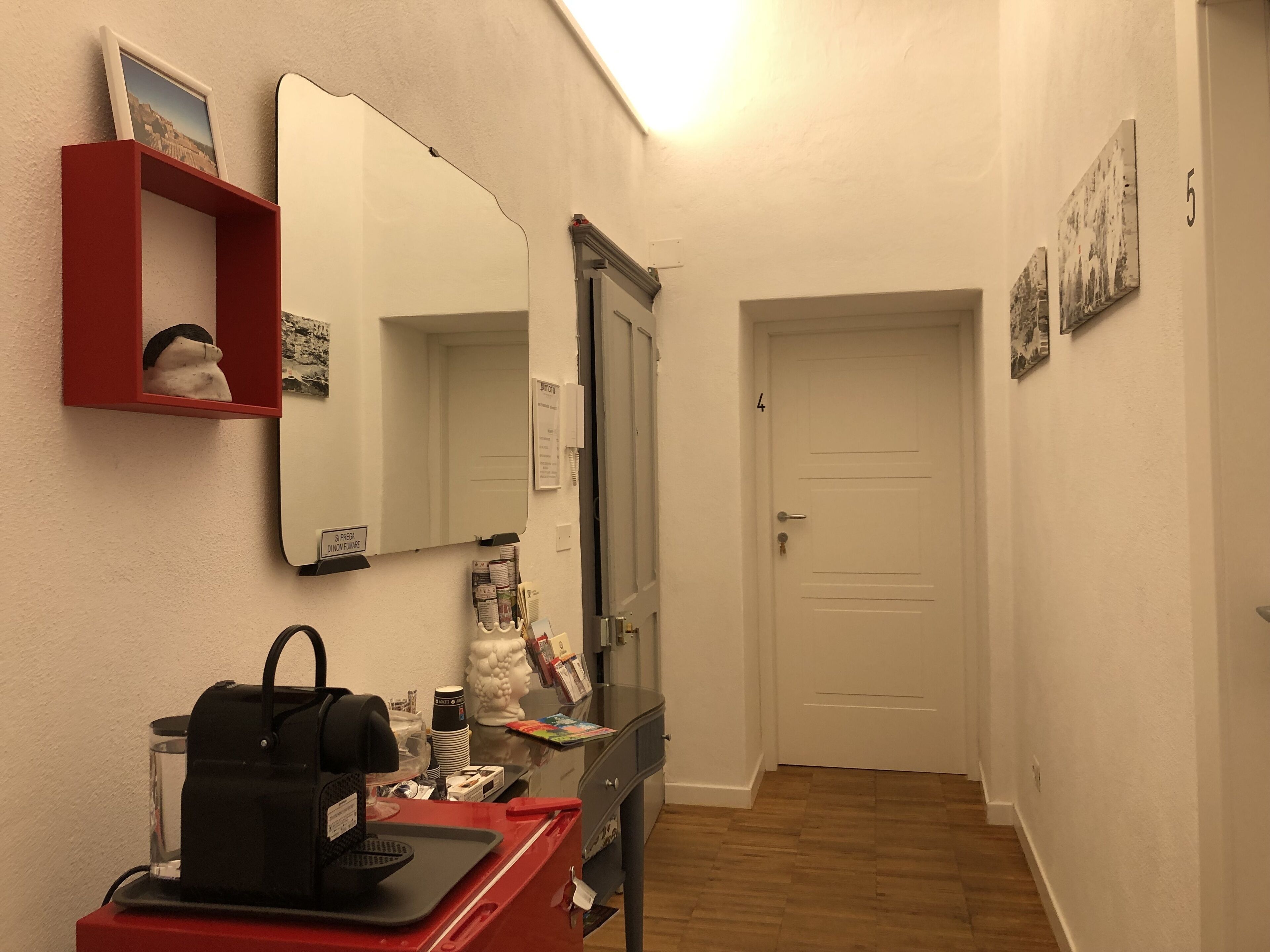 Un pasillo con un escritorio rojo, una cafetera negra, una escultura de busto blanco y una puerta con el número 4.